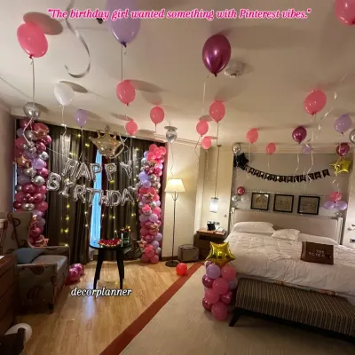 A full view of this Pinterest-worthy birthday setup. The room is filled with pink, purple, and silver balloons, with two beautiful balloon columns framing the "Happy Birthday" banner and fairy lights.