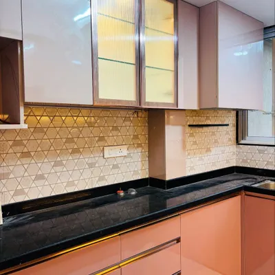 A modern L-shaped kitchen with a beautiful dual-tone design. The lower cabinets are a matte salmon pink with gold-accented handles, while the upper cabinets mix solid panels with fluted glass doors and a geometric backsplash.