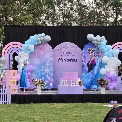A complete stage setup for a 'Frozen' themed birthday party. The design features custom arched backdrops with characters, a themed cake stand, and balloon garlands that mimic a snowy landscape.