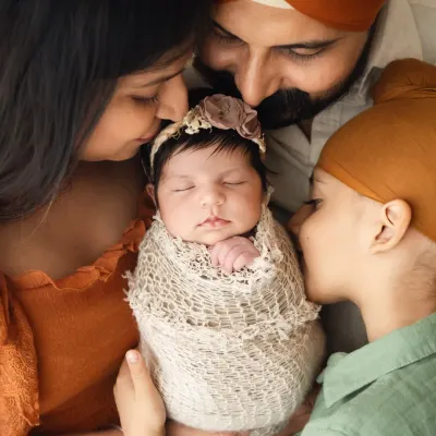 A beautiful close-up of a family of four, with both parents and a big brother kissing the newborn baby. This is a classic pose for a newborn with sibling photoshoot.