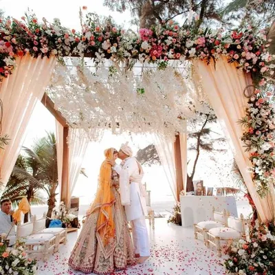 A breathtaking beachside mandap for a destination wedding in Goa, where the couple exchanges vows under a canopy of lush florals with the Arabian Sea as their witness. This is the epitome of a romantic, luxury wedding ceremony.