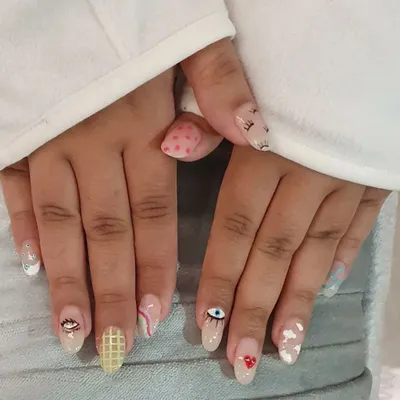 A fun, mismatched manicure showcasing a variety of hand-painted designs, including evil eyes, clouds, hearts, and geometric patterns.