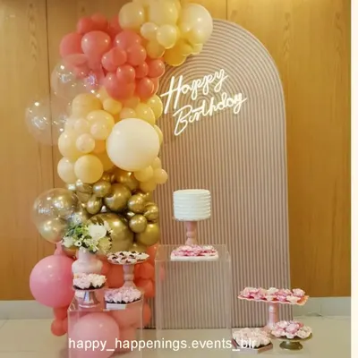 This minimalist birthday setup features a soft pink ribbed arch panel with a delicate neon sign. The organic balloon garland in pastel pink, peach, and gold adds a touch of color without overwhelming the clean, modern aesthetic.