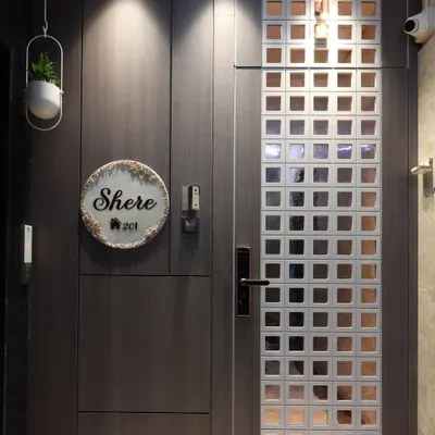 A modern entrance featuring a dark wood-finish main door and a contrasting white safety door with a square grid pattern. The design is complemented by a custom nameplate and focused downlights for a warm welcome.