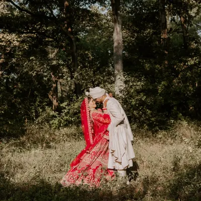 A romantic kiss in the middle of a forest in Austin, Texas. The bride's vibrant red lehenga against the green woods creates a stunning, fairytale-like image.