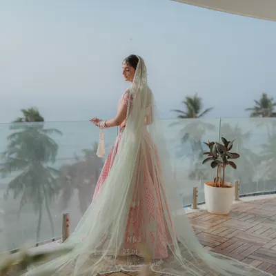 A breathtaking shot of the bride on a balcony overlooking the ocean, her long veil flowing in the breeze. A truly cinematic bridal portrait.