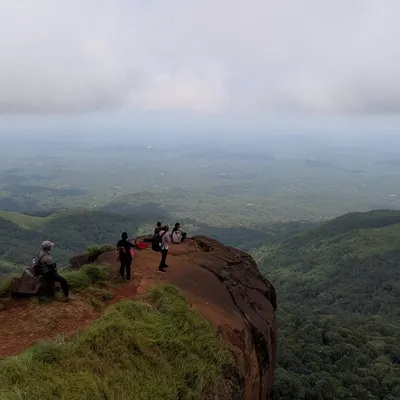 A group of trekkers on a cliff edge, enjoying the panoramic views from Kurinjal Peak.