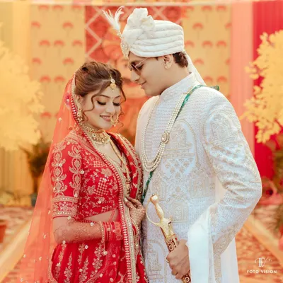 A classic portrait of the couple in their wedding attire, the bride in a traditional red lehenga and the groom in a white sherwani, capturing their regal presence.