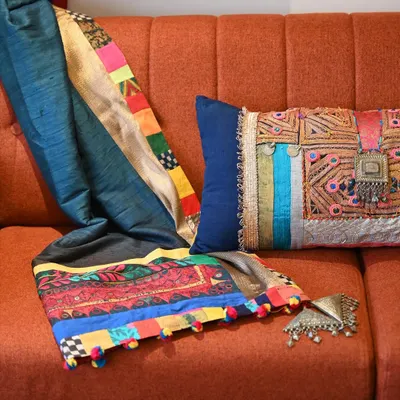 A custom-made Banjara throw and lumbar cushion set, designed to add a burst of festive color. The vintage Banjara textile is richly embellished with old jewelry, coins, and tassels, turning it into a statement piece for the sofa.
