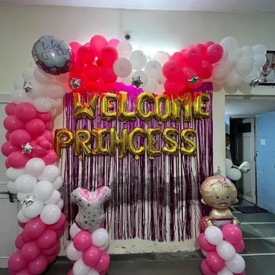 A complete "Welcome Princess" decoration for a baby girl's homecoming. This setup features a vibrant pink and white balloon arch, gold foil letters, and a shimmering purple tinsel curtain for a festive photo backdrop.