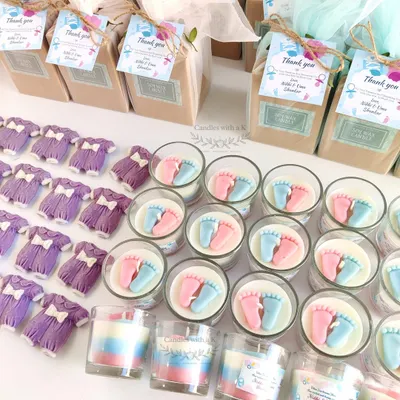 A complete baby shower return gift set, featuring a layered votive candle with tiny pink and blue baby feet, and a matching baby onesie wax sachet.