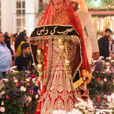 Veiled in majesty, this bride shines in an eternal red lehenga for her Nikah. The personalized veil adds a layer of heritage, making her entrance truly unforgettable.