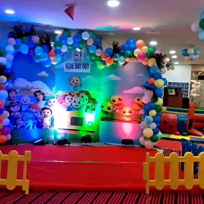 A vibrant Cocomelon stage setup for a "Kid's Day Out" event. This decoration features a large, colorful printed backdrop with all the favorite characters, framed by a playful balloon arch.