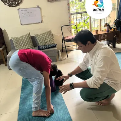 I am providing a gentle adjustment to a client in a forward fold (Uttanasana). This hands-on assist helps her deepen the stretch safely and release tension in her hamstrings and lower back.