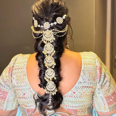 A stunning messy braid adorned with a beautiful, cascading hair ornament. This is a perfect hairstyle for a sangeet or reception, combining traditional and modern elements.