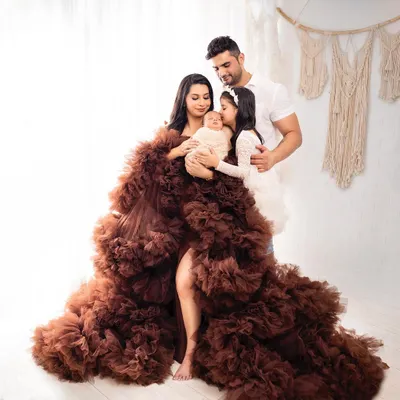 A stunning family portrait featuring the mother in a dramatic ruffled gown, holding her newborn while the father and older sister look on. This is a perfect example of a full family newborn photoshoot.