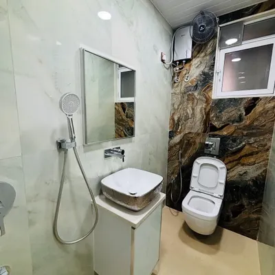 A full view of a remodeled bathroom. The design features a combination of light marble-finish wall tiles and a dramatic, dark-veined accent wall behind the wall-mounted toilet.