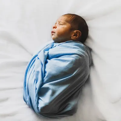 A beautifully simple newborn portrait. This baby boy is swaddled snugly in blue on a clean white background, emphasizing his peaceful, sleeping form.