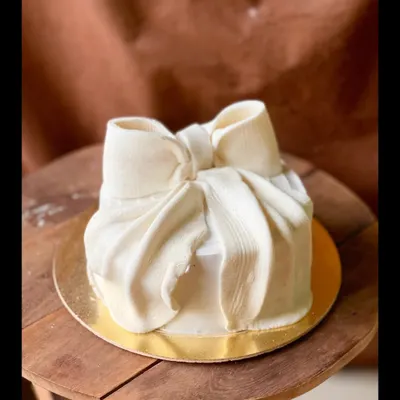 A cake designed to look like a perfectly wrapped gift. This stunning piece features a large, sculpted white chocolate bow on a smooth, square cake.