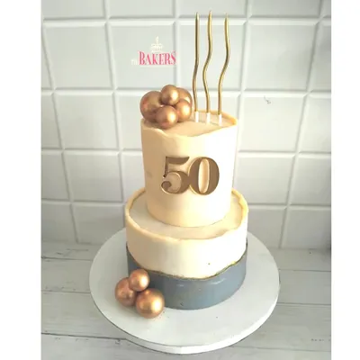 An elegant two-tier cake for a 50th birthday celebration. This no-fondant design features a modern, minimalist aesthetic with a concrete-grey bottom tier and a clean white top tier, accented with gold spheres and a bold "50" topper.