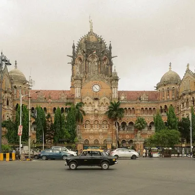 A classic Kaali-Peeli taxi drives past the magnificent Chhatrapati Shivaji Maharaj Terminus. This single frame perfectly unites two of Mumbai's most iconic symbols of transport and architecture.