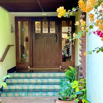 The entrance to Roopa Hariprasad’s Residence features a custom-designed wooden door with intricate glasswork. The steps are adorned with traditional patterned tiles, creating a welcoming and highly personal entryway.