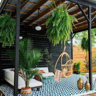 An inspirational design for a covered terrace or patio. This concept uses patterned floor tiles, a dark pergola structure, and lush hanging plants to create a stylish and shaded outdoor lounge.