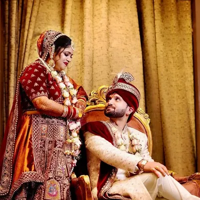 A regal wedding portrait of the couple. The groom is seated while the bride stands beside him, creating a classic and royal composition.
