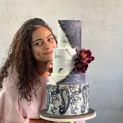 Here I am with a stunning three-tiered wedding cake I created during a masterclass. It features intricate paisley stenciling, a marble effect, and beautiful handmade sugar flowers. I'm excited to bring these techniques to your special cake.