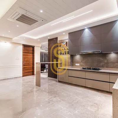 An open-plan kitchen with a breakfast bar that separates it from the living area. The sleek, handleless cabinets in grey and beige tones are complemented by the polished marble floor that runs throughout the space.