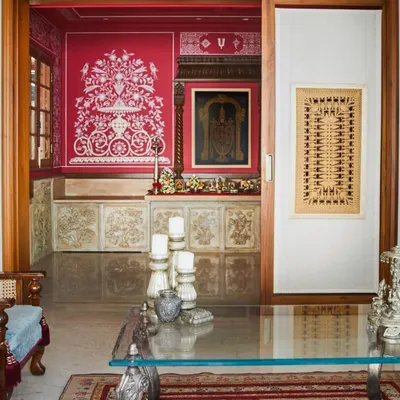 A glimpse into the striking red home temple in Hyderabad. The view from the living room reveals a space that is intensely spiritual, with hand-painted walls and carved details creating a powerful sanctuary within the home.