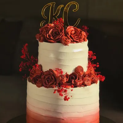A stunning two-tier engagement cake with a red ombre buttercream finish and handcrafted red roses. The custom 'KC' topper makes it a truly personal centerpiece for a special celebration.