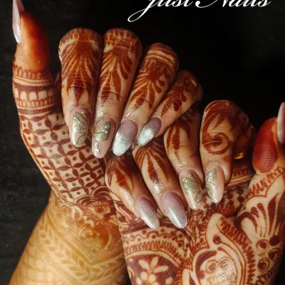 A stunning example of bridal nails designed to complement intricate henna. This set features long, almond-shaped extensions with a mix of silver glitter and delicate, hand-painted leaf patterns.