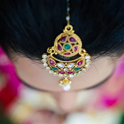 A top-down macro shot of a bride's 'maang tikka', highlighting the beautiful kundan and gemstone work in her wedding jewelry.