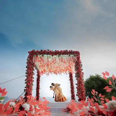 A truly epic destination wedding shot. The couple shares a kiss under a magnificent floral mandap, set against the sky and sea. This is what destination wedding dreams are made of.