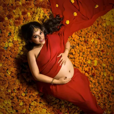 In full bloom. This stunning overhead shot shows the mother-to-be lying on a bed of vibrant marigolds, her red saree spreading out like a flower. It's a modern, artistic take on a traditional theme.