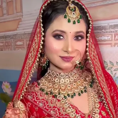 A full view of a classic red bridal look available for rent. This set includes a gold-plated choker with green accents, a matching maang tikka, and a simple nath.