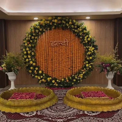 This is a classic Haldi setup for an indoor event. We used a large circular backdrop made entirely of marigold strings and a floral border, with two traditional brass urlis for the ceremony.