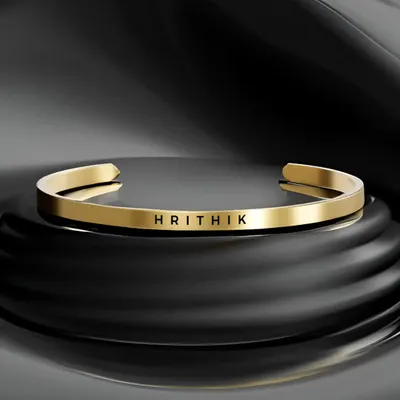 A stunning product shot of the gold-plated cuff bracelet, professionally engraved with the name 'HRITHIK'. The clean font and polished finish create a bold, elegant look.