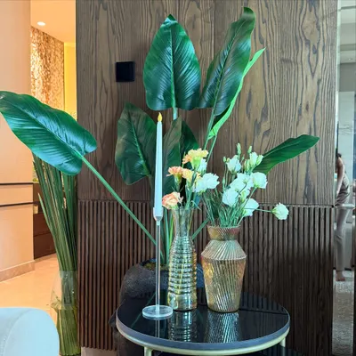 For this housewarming in a luxurious Noida home, we placed a simple yet elegant arrangement on a side table. The combination of fresh white flowers, large green leaves, and a single candle complements the modern wood-paneled wall perfectly.