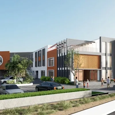 This wide view shows the KPS School from the main road, illustrating how the building sits within its environment. The design strategically uses different materials and forms, like the pixelated graphic on the orange wall and the vertical fins, to create a visually engaging and modern educational facility.