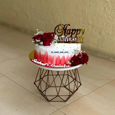 A beautiful anniversary cake with a red ombre design, fresh red roses, and a golden "Happy Anniversary" topper.