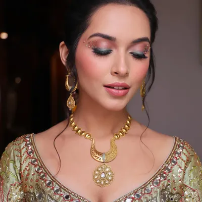 A close-up of the carnival-inspired Mehendi makeup. The eyes are the focus, with a blend of pink and green eyeshadow, a sharp wing, and delicate gold dust and studs for a truly unique look.