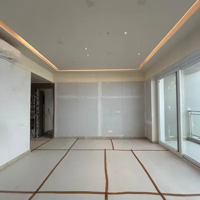 A blank canvas full of potential. This is a work-in-progress shot of a living room, with floor-to-ceiling windows promising abundant light. The markings on the floor map out the future placement of furniture, the first step in transforming this empty shell into a home.