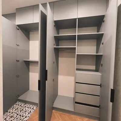 This open hinged wardrobe shows a practical layout with double hanging rods, multiple shelves, and a bank of four deep drawers. The cool grey finish and handleless design give it a clean, modern aesthetic.