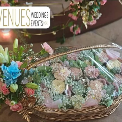 A beautiful wicker basket filled with a lush arrangement of pastel-colored fresh flowers. This type of floral gift basket serves as a stunning welcome gift or a centerpiece for guest tables.
