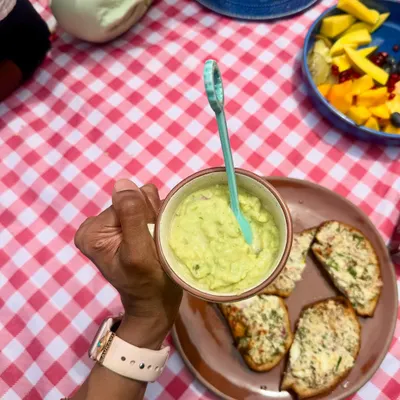 Holding a cup of creamy avocado pudding during a picnic, a healthy fat and fiber-rich snack to accompany our high-protein chilli cheese toast.
