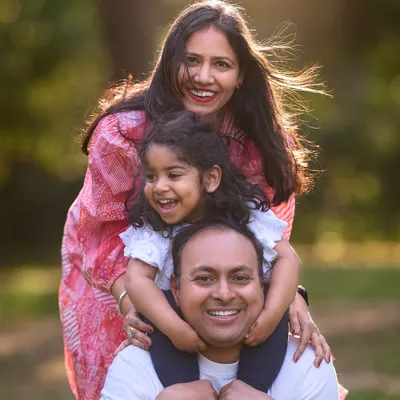 A beautiful family portrait where everyone's personality shines through. The layered pose with their daughter on her father's shoulders creates a lovely sense of closeness and joy.