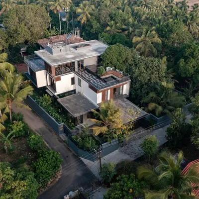 An aerial view and a dusk shot of the Mango Tree Yard residence in Thrissur, showing the pavilion-style layout nestled within a lush, tropical landscape.