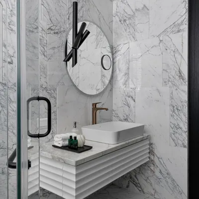 This bathroom makeover is all about bliss where design and comfort unite. The space is clad in dramatic veined marble, with a custom fluted vanity and a sculptural mirror, transforming it into a sleek and modern sanctuary.